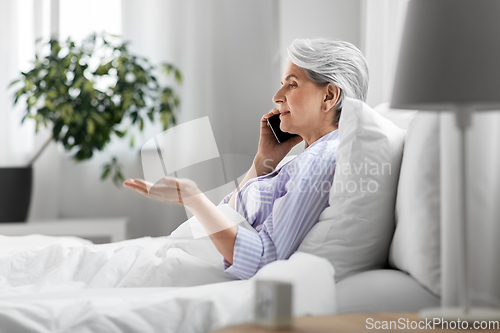 Image of senior woman calling on smartphone in bed at home
