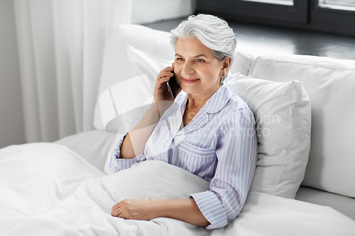 Image of senior woman calling on smartphone in bed at home