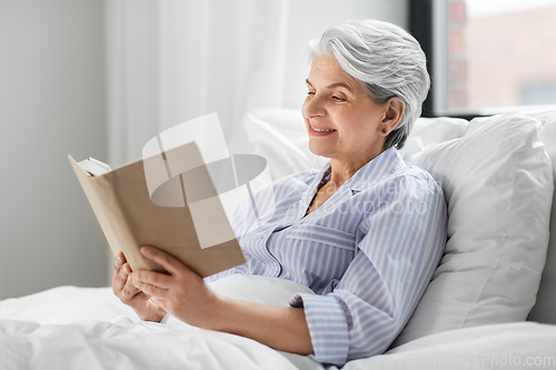 Image of senior woman reading book in bed at home bedroom