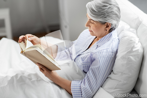 Image of senior woman reading book in bed at home bedroom