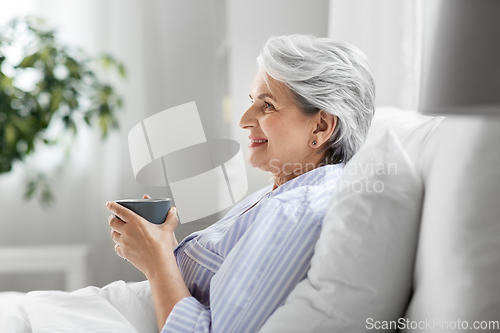 Image of old woman with cup of coffee in bed at home