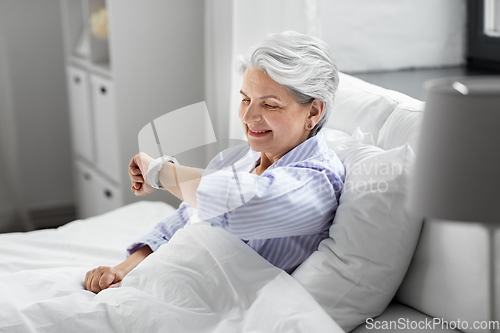 Image of happy senior woman sitting in bed at home bedroom