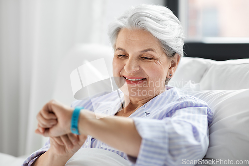 Image of happy old woman with health tracker sitting in bed