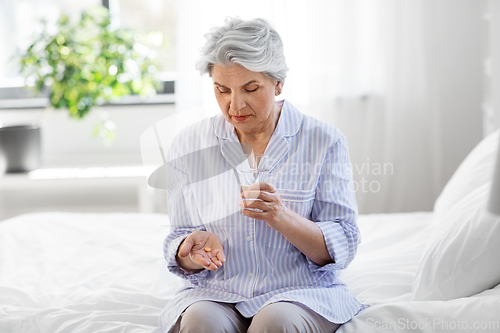 Image of senior woman with pill and water sitting on bed