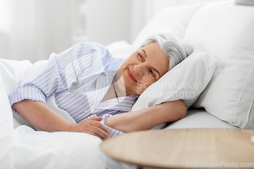 Image of happy senior woman lying in bed at home bedroom