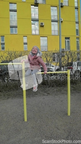 Image of little girl hanging on a sports horizontal bar on the street near the house. child playing in the playground