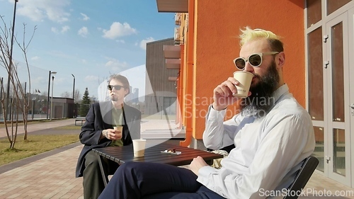 Image of Loving gay couple sitting outdoors together and drinking coffee. Two handsome men having romantic date in park. LGBT concept