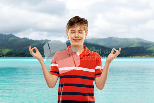 Image of happy smiling meditating boy over hills and ocean