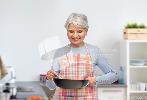 Image of smiling senior woman with frying pan at kitchen