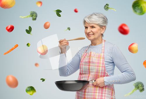 Image of smiling senior woman in apron with frying pan