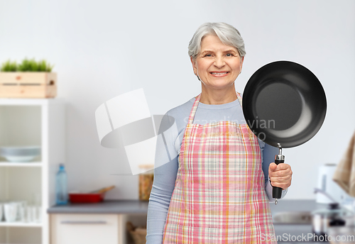 Image of smiling senior woman with frying pan at kitchen