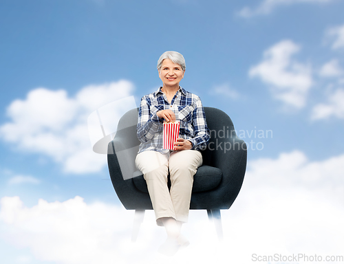 Image of senior woman eating popcorn sitting in armchair