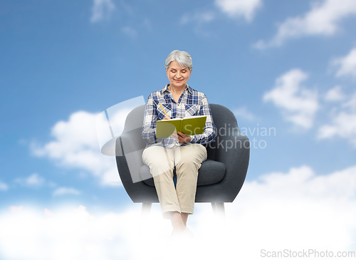 Image of smiling senior woman in armchair writing to diary