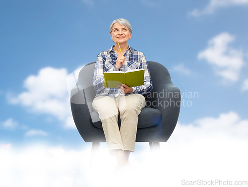 Image of smiling senior woman in armchair writing to diary