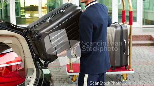 Image of Bellboy taking baggage of guest from thee car to his room