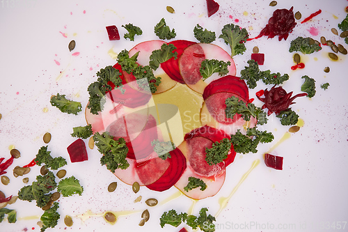 Image of Carpaccio of beet and pear with pumpkin seeds decorated with sauce and green leaves.