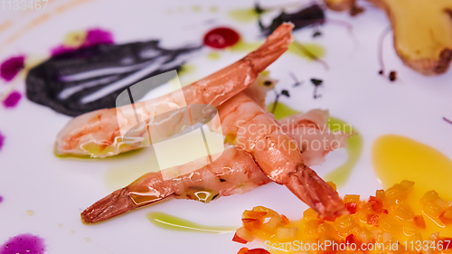 Image of three prawns on a white table decorated with chopped vegetables and sauce.