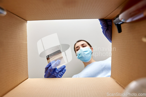 Image of woman in mask unpacking parcel box with hair bands