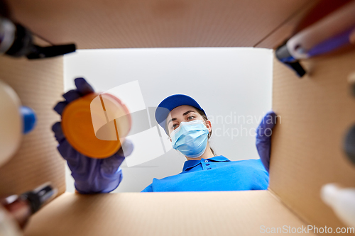 Image of woman in mask packing parcel box with cosmetics