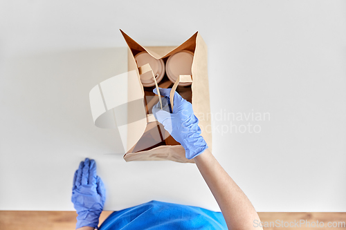 Image of delivery woman in gloves packing food and drinks