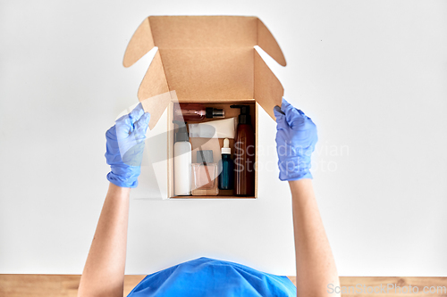 Image of hands in gloves packing parcel box with cosmetics