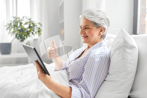 Image of old woman with tablet pc having video call in bed