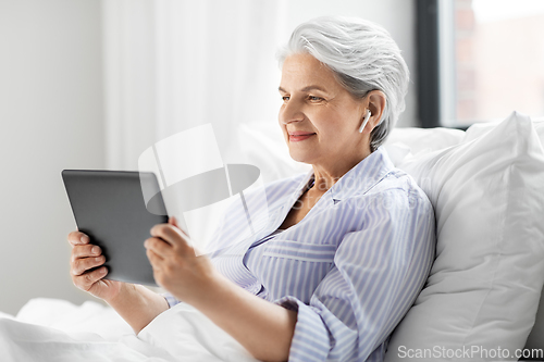 Image of senior woman with tablet pc and earphones in bed