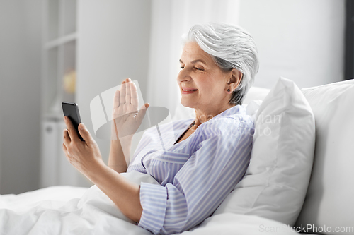 Image of senior woman with phone having video call in bed