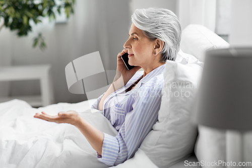 Image of senior woman calling on smartphone in bed at home