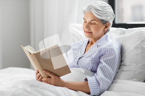 Image of senior woman reading book in bed at home bedroom