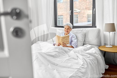 Image of senior woman reading book in bed at home bedroom