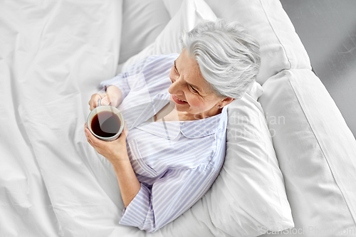 Image of old woman with cup of coffee in bed at home