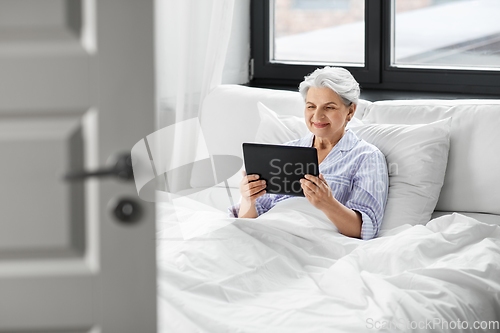 Image of happy senior woman with tablet pc in bed at home