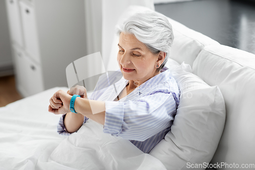 Image of happy old woman with health tracker sitting in bed