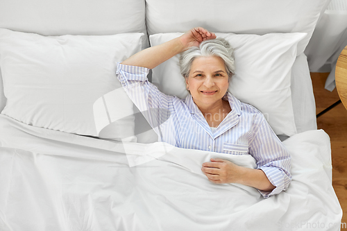 Image of smiling senior woman lying in bed at home bedroom