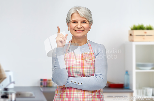 Image of smiling senior woman pointing finger up at kitchen