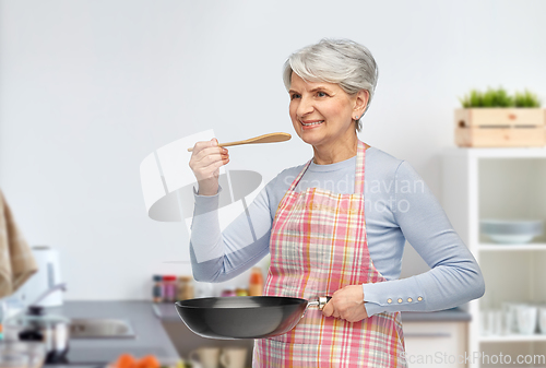 Image of smiling senior woman with frying pan at kitchen