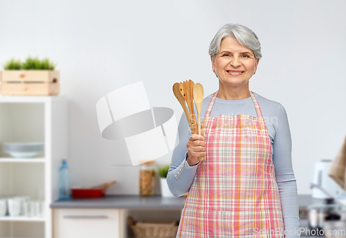 Image of smiling senior woman with wooden spoons at kitchen