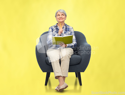 Image of smiling senior woman in armchair writing to diary