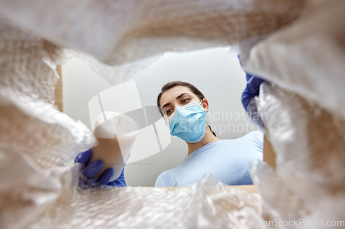 Image of woman in mask packing candles into parcel box