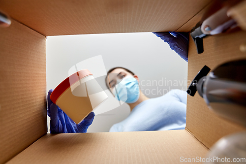 Image of woman in mask unpacking parcel box with cosmetics