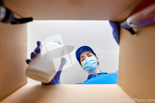 Image of woman in mask packing parcel box with cosmetics