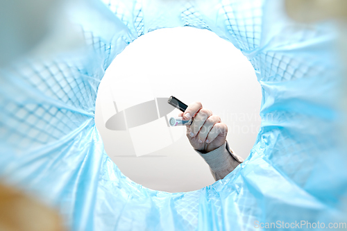 Image of hand throwing alkaline batteries into trash can