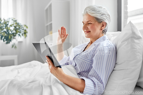 Image of old woman with tablet pc having video call in bed