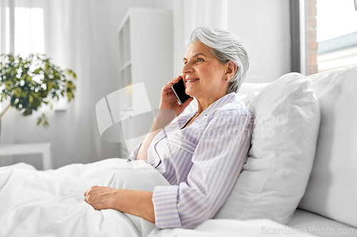 Image of senior woman calling on smartphone in bed at home