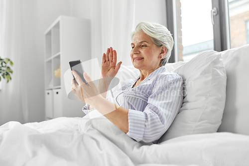 Image of senior woman with phone having video call in bed