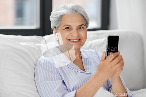 Image of senior woman with smartphone and earphones in bed