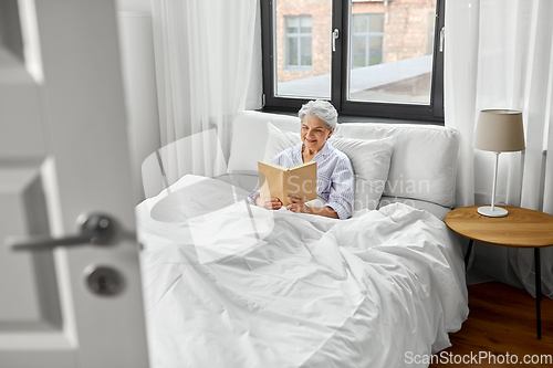 Image of senior woman reading book in bed at home bedroom