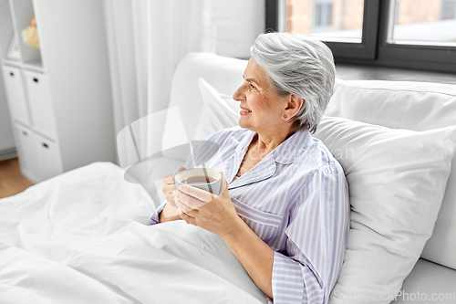 Image of old woman with cup of coffee in bed at home