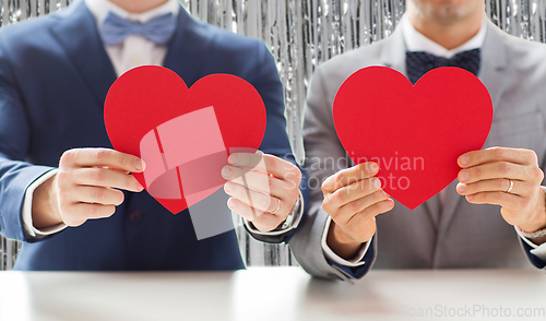 Image of close up of male gay couple holding red hearts